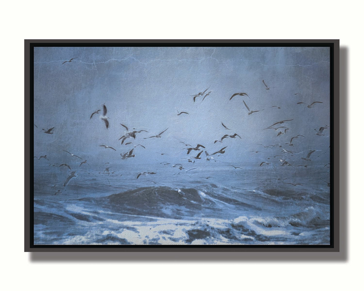 An edited photo of a flock of seagulls swarming over the sea in search of food, as the sky darkens and the waves pick up with an oncoming storm. Printed on canvas in a float frame.