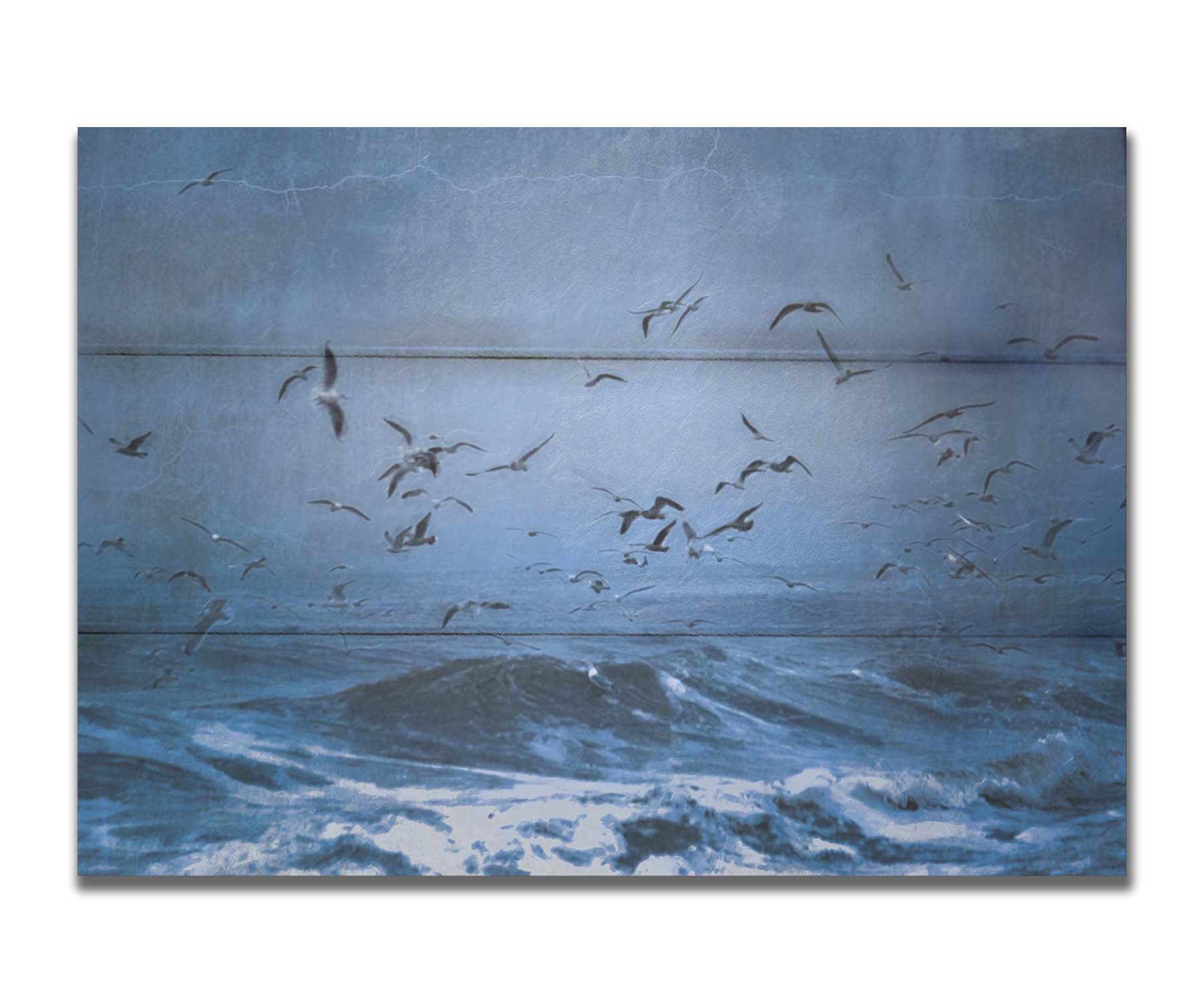 An edited photo of a flock of seagulls swarming over the sea in search of food, as the sky darkens and the waves pick up with an oncoming storm. Printed on a box board.