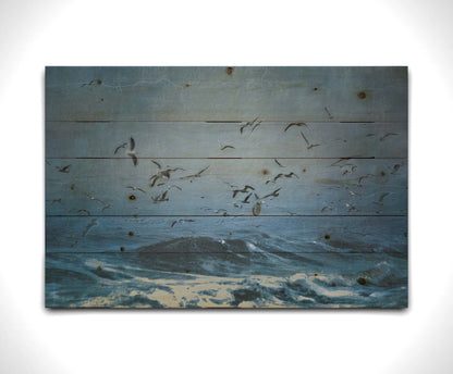 An edited photo of a flock of seagulls swarming over the sea in search of food, as the sky darkens and the waves pick up with an oncoming storm. Printed on a wood pallet.