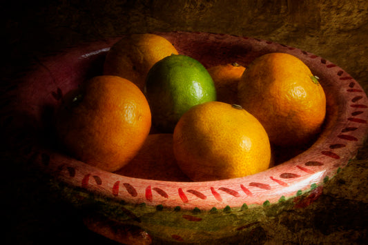 A photo of a bowl of oranges, with one lime placed in the center.