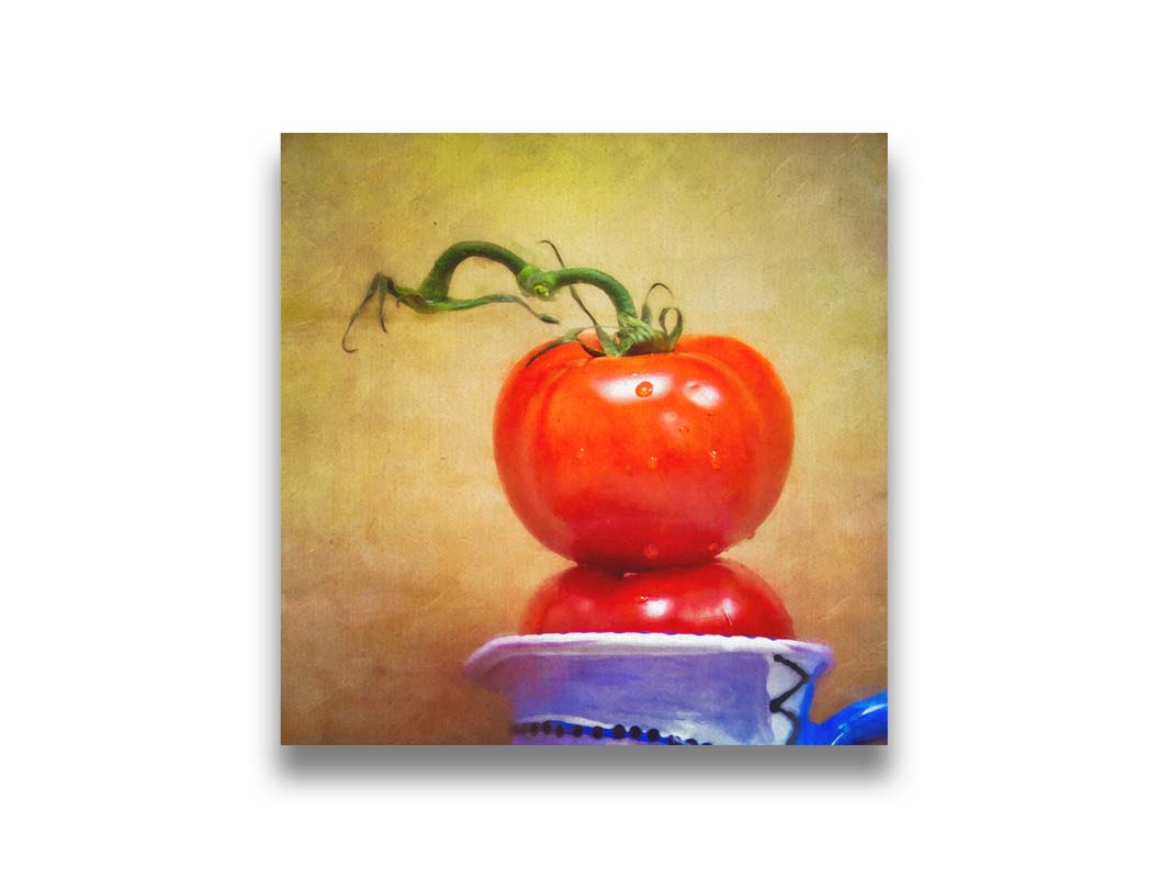 A photograph of bright red tomatoes stacked inside a blue and white ceramic cup, set against a textured neutral background. Printed on canvas.