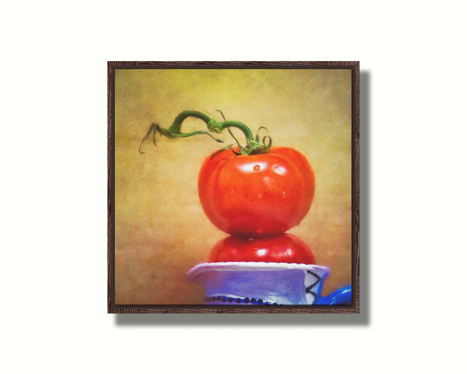 A photograph of bright red tomatoes stacked inside a blue and white ceramic cup, set against a textured neutral background. Printed on canvas in a float frame.