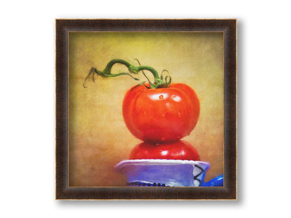 A photograph of bright red tomatoes stacked inside a blue and white ceramic cup, set against a textured neutral background. Printed on canvas and framed.