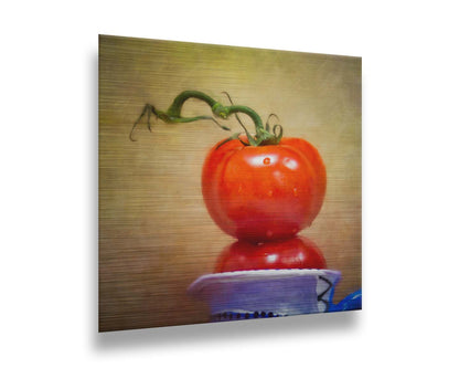 A photograph of bright red tomatoes stacked inside a blue and white ceramic cup, set against a textured neutral background. Printed on metal.