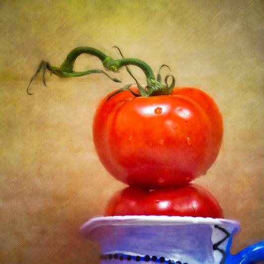 A photograph of bright red tomatoes stacked inside a blue and white ceramic cup, set against a textured neutral background.