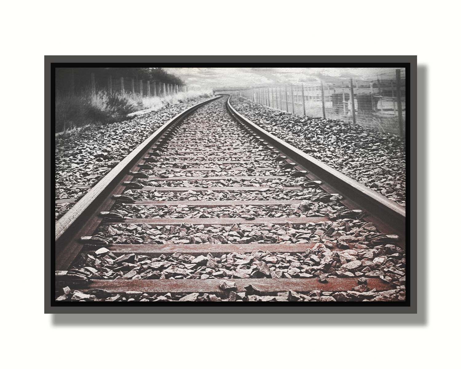 A photo looking down train tracks in black and white, with tinges of red-brown spot color. Printed on canvas in a float frame.