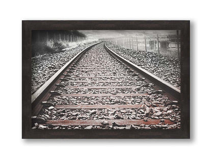 A photo looking down train tracks in black and white, with tinges of red-brown spot color. Printed on canvas and framed.