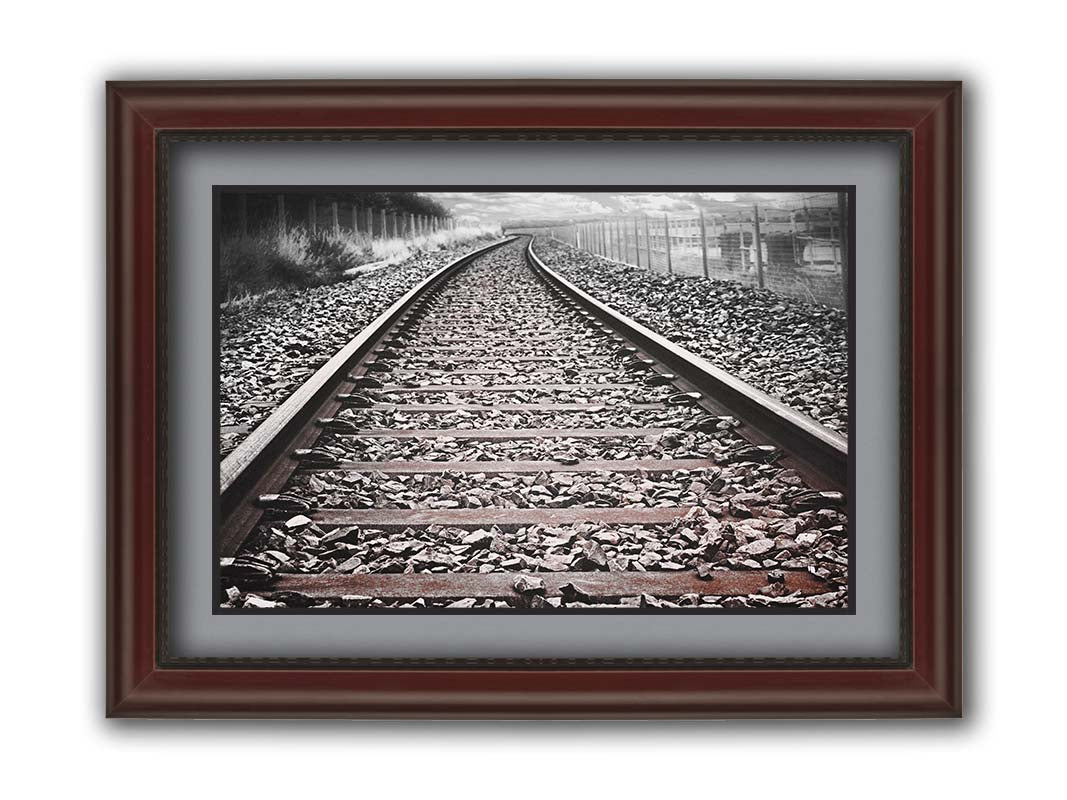 A photo looking down train tracks in black and white, with tinges of red-brown spot color. Printed on paper, matted, and framed.