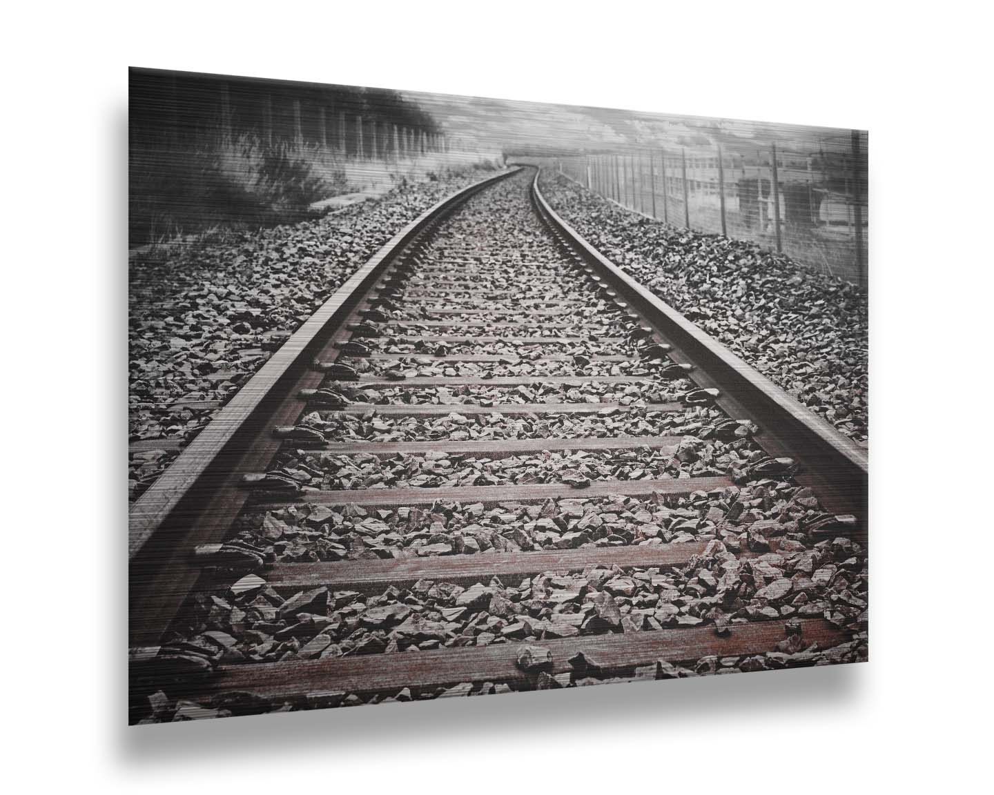 A photo looking down train tracks in black and white, with tinges of red-brown spot color. Printed on metal.