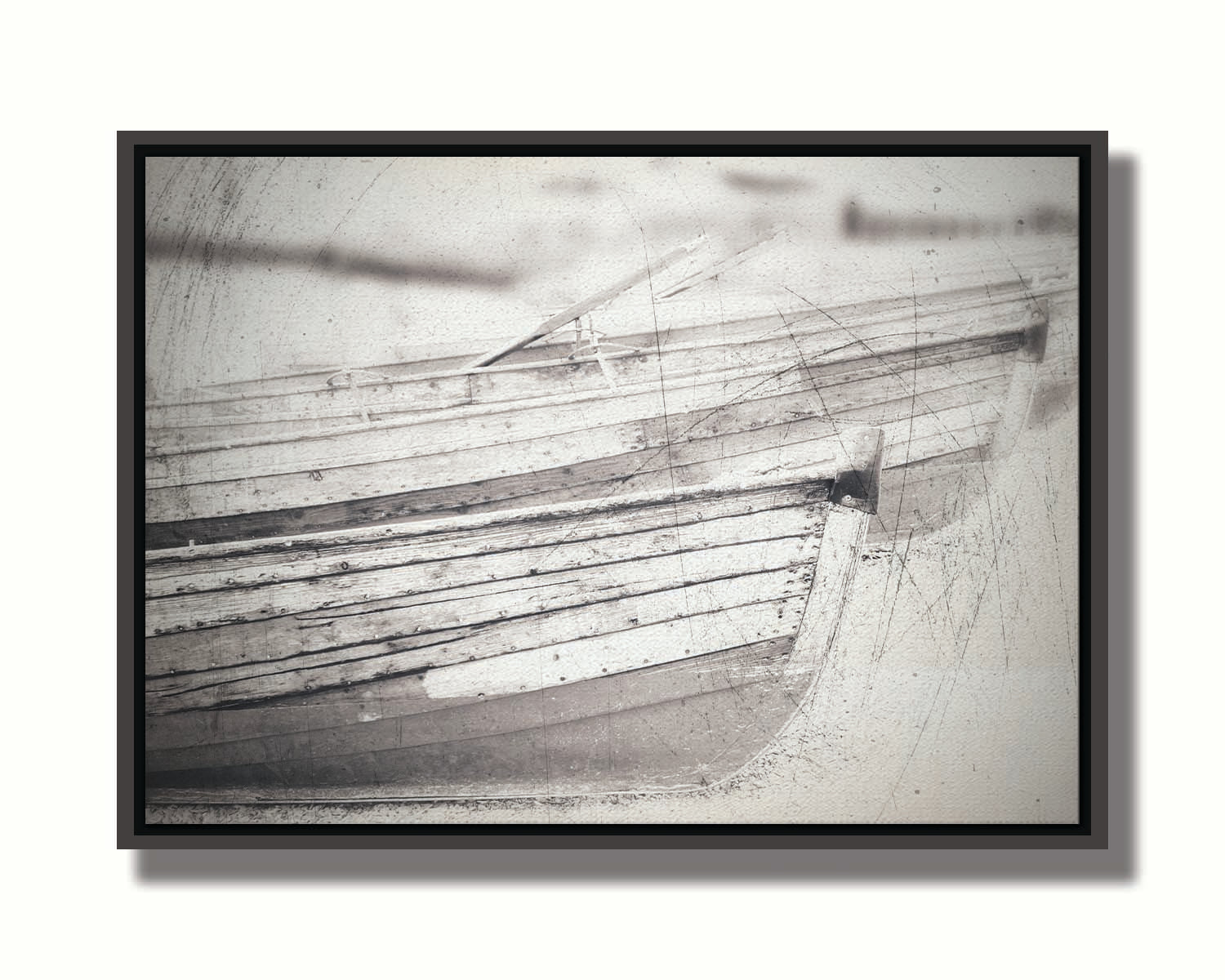 A grayscale photo of two rowboats on the sand. It is overlayed with a scratchy weathered texture. Printed on canvas in a float frame.