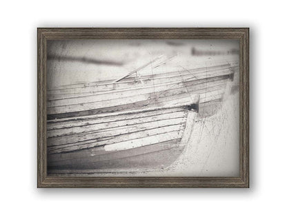 A grayscale photo of two rowboats on the sand. It is overlayed with a scratchy weathered texture. Printed on canvas and framed.