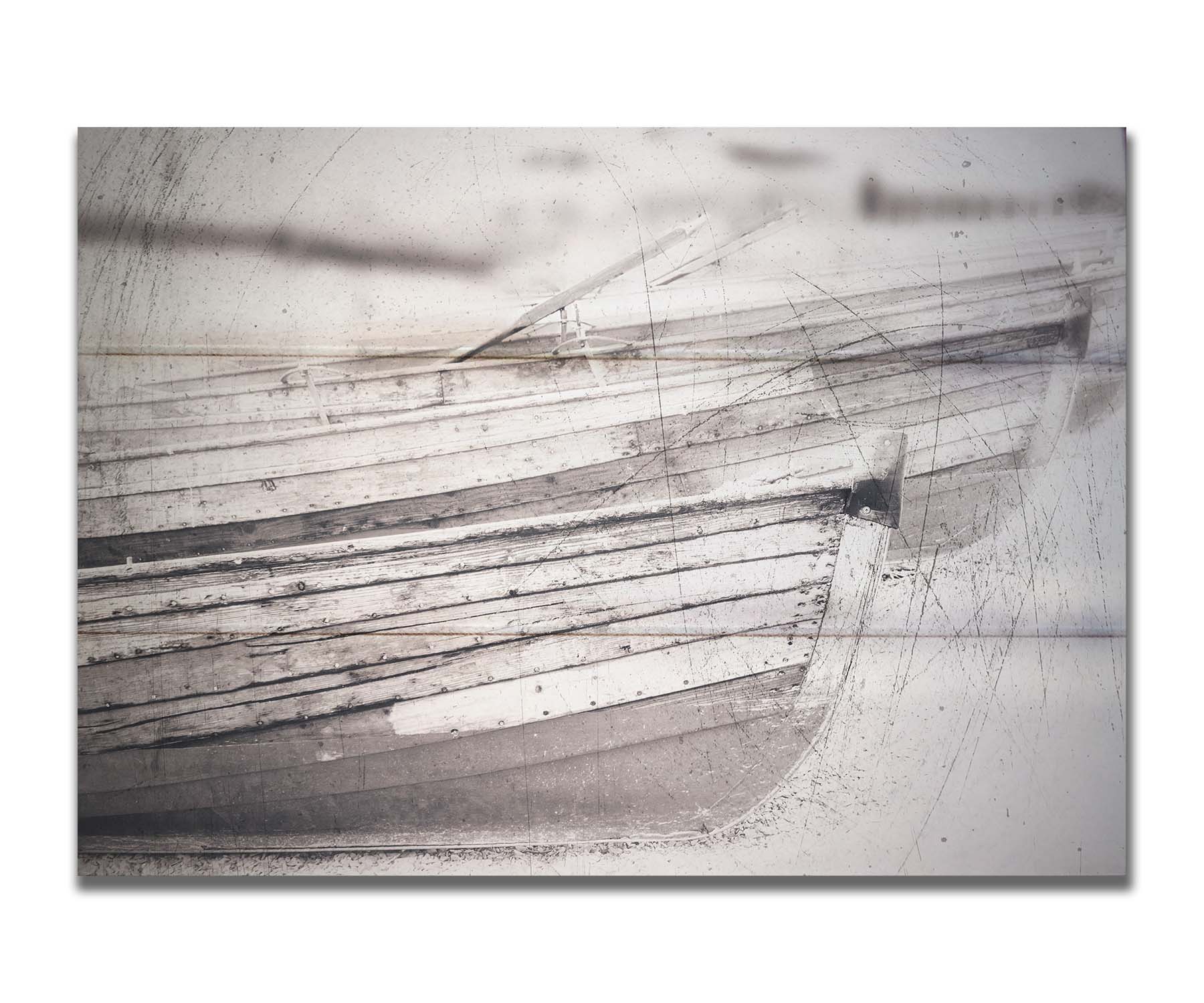 A grayscale photo of two rowboats on the sand. It is overlayed with a scratchy weathered texture. Printed on a box board.