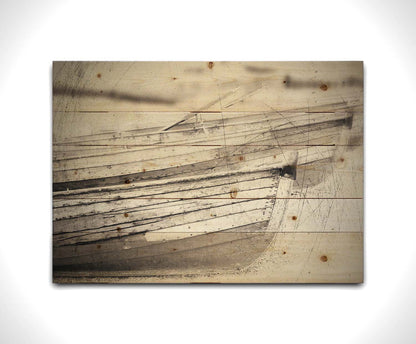 A grayscale photo of two rowboats on the sand. It is overlayed with a scratchy weathered texture. Printed on a wood pallet.