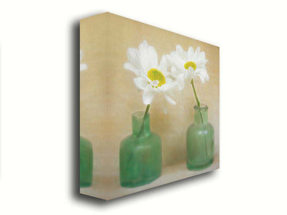 A photo of two white flowers in green glass jars, sitting against one another against a tan backdrop. Printed on canvas.