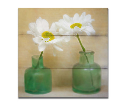 A photo of two white flowers in green glass jars, sitting against one another against a tan backdrop. Printed on a box board.