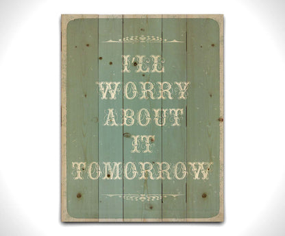 A typography design reading "I'll worry about it tomorrow" in white on a pale blue background. Printed on a wood palelt.