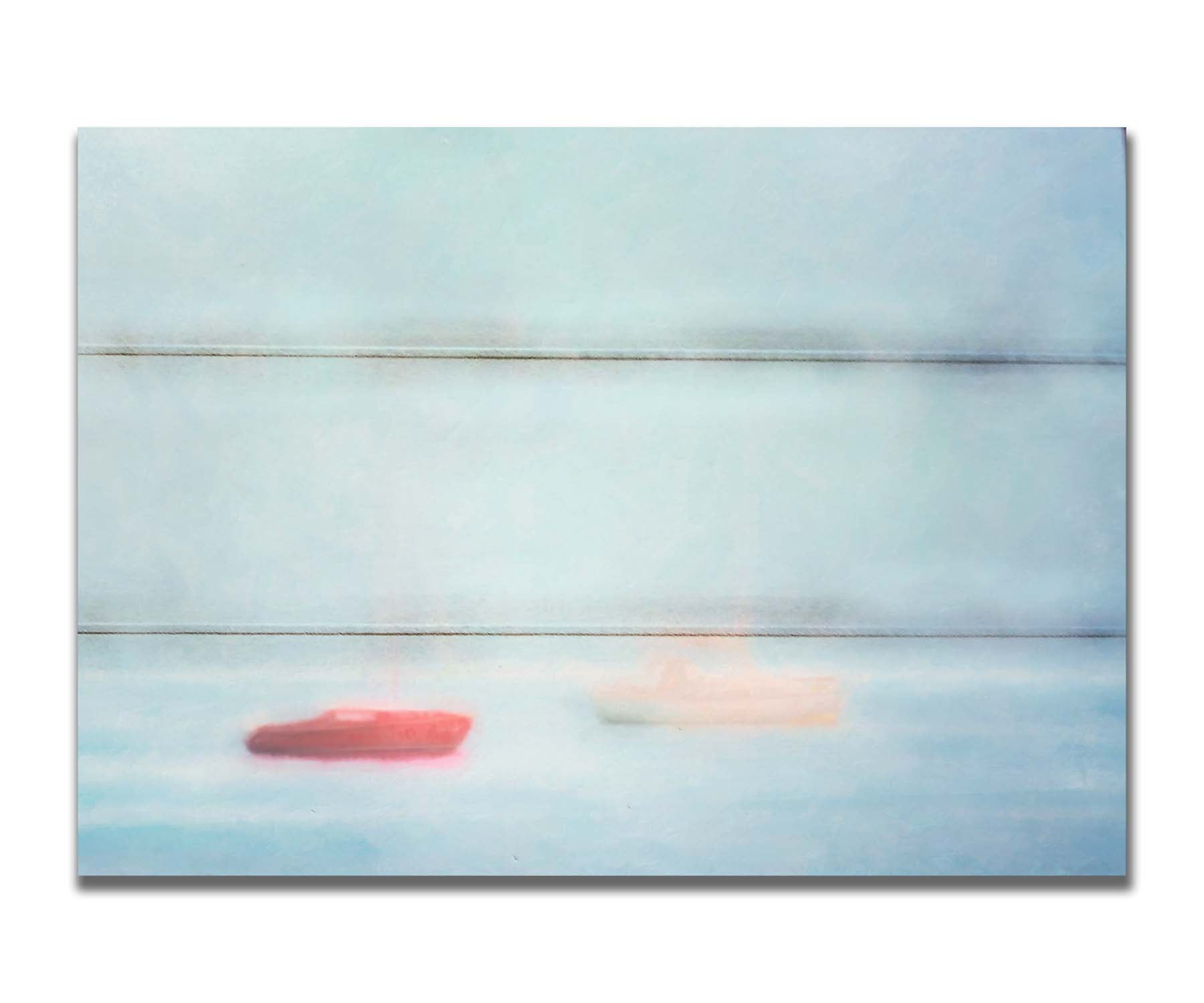 A photo of a small red boat and a small white and yellow boat floating at sea. The photo is edited to have a soft, blurry quality which blends the sky and sea together on the horizon. Printed on a box board.