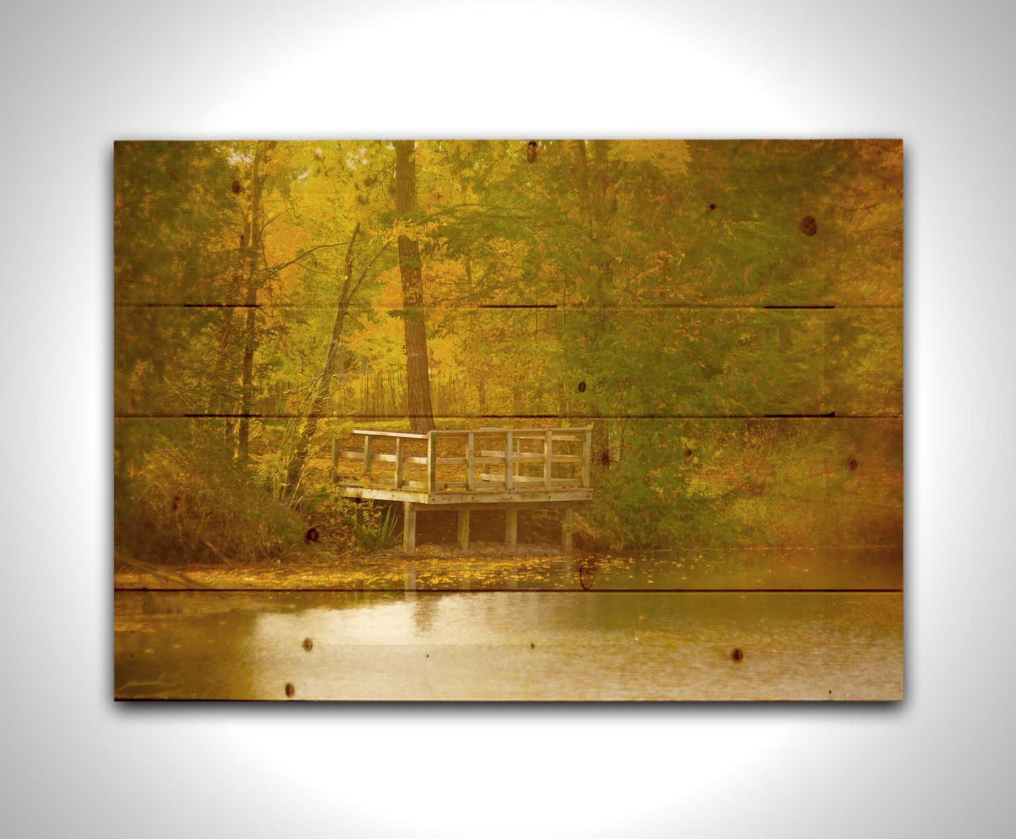 A photo of a small wooden dock, overlooking a forest lake during autumn. Yellow leaves cover the trees and ground, and float atop the water. Printed on a wood pallet.