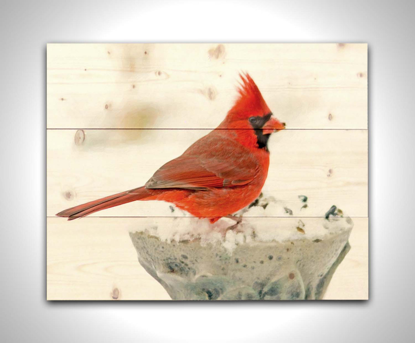 A photograph of a bright red cardinal, perched on a snowy post, eating seeds. Printed on a wood pallet.