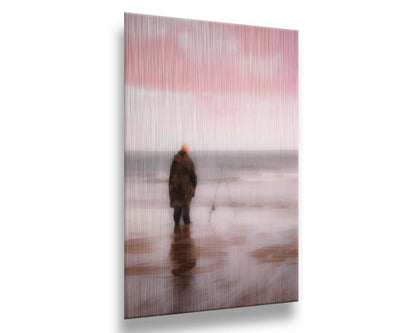 A photograph of a fisherman in oilskins standing in the shallows of the ocean, watching his fishing pole propped up beside him. Printed on metal.