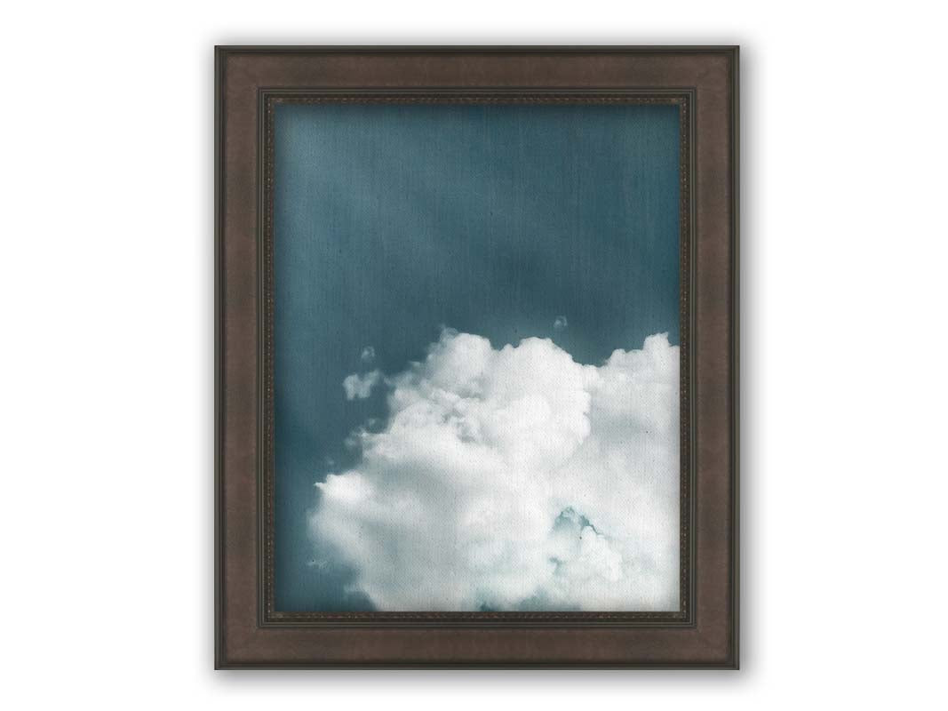 An edited photo of a soft white cloud against a steely blue background. Printed on canvas and framed.