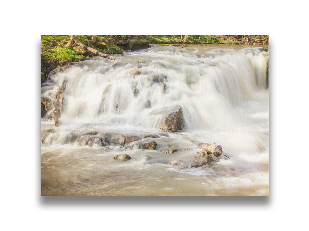 A photograph of a small river waterfall, only a few feet high. The use of a slow shutter speed technique gives the water a soft, gentle appearance. Printed on canvas.