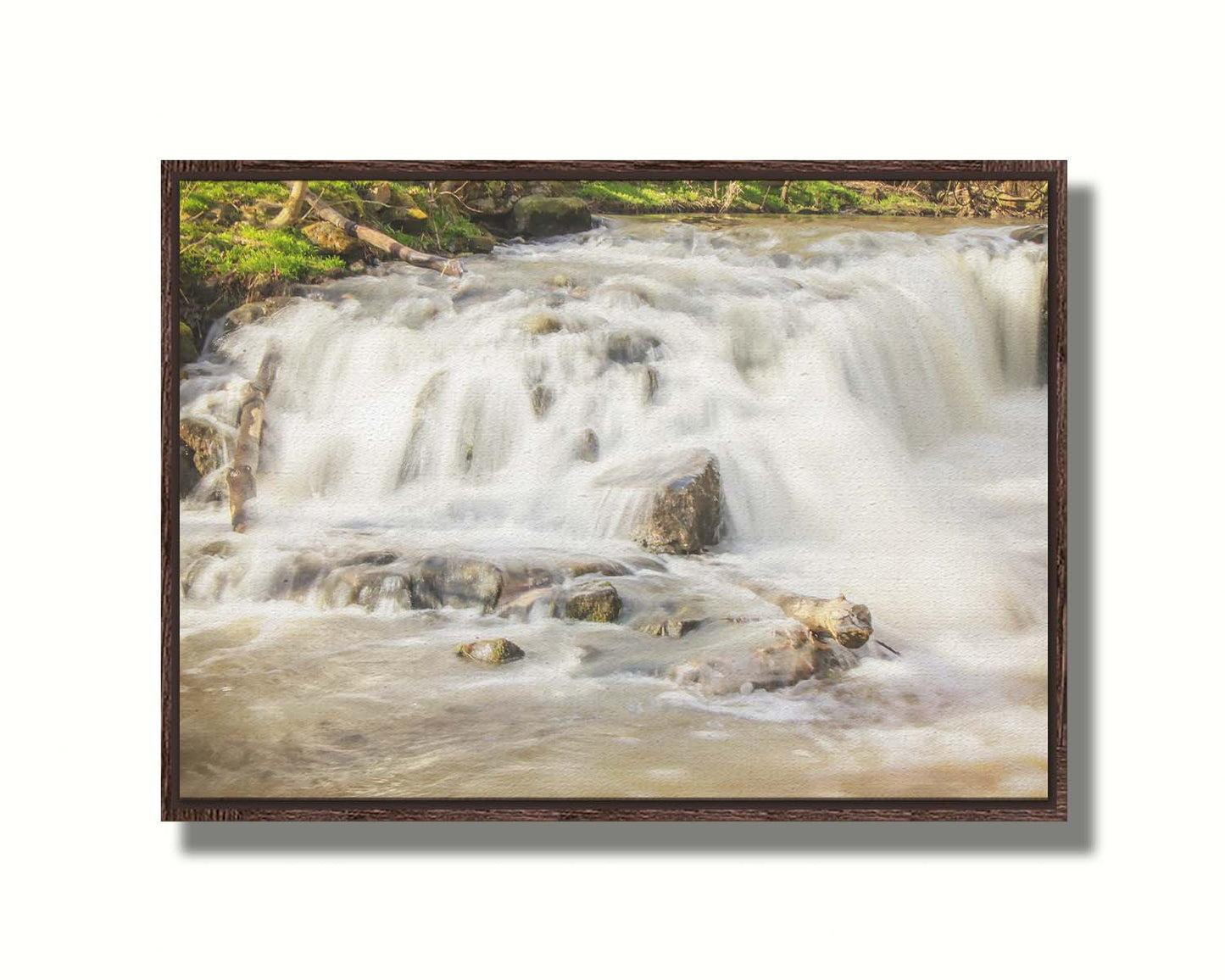 A photograph of a small river waterfall, only a few feet high. The use of a slow shutter speed technique gives the water a soft, gentle appearance. Printed on canvas in a float frame.