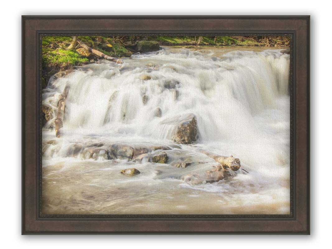 A photograph of a small river waterfall, only a few feet high. The use of a slow shutter speed technique gives the water a soft, gentle appearance. Printed on canvas and framed.