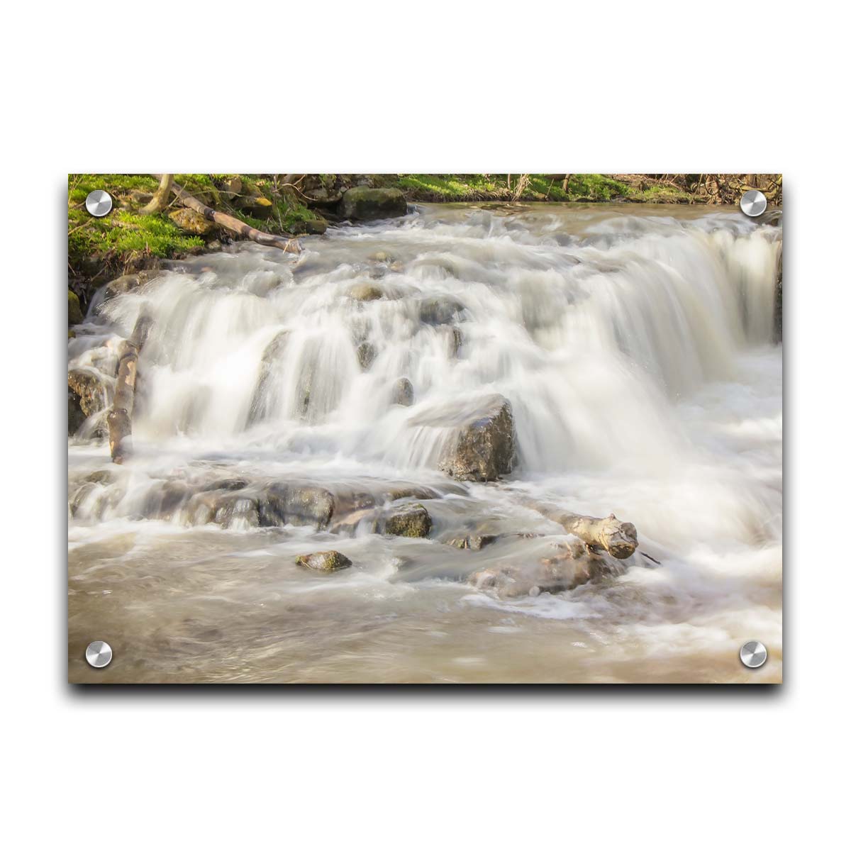 A photograph of a small river waterfall, only a few feet high. The use of a slow shutter speed technique gives the water a soft, gentle appearance. Printed on acrylic.