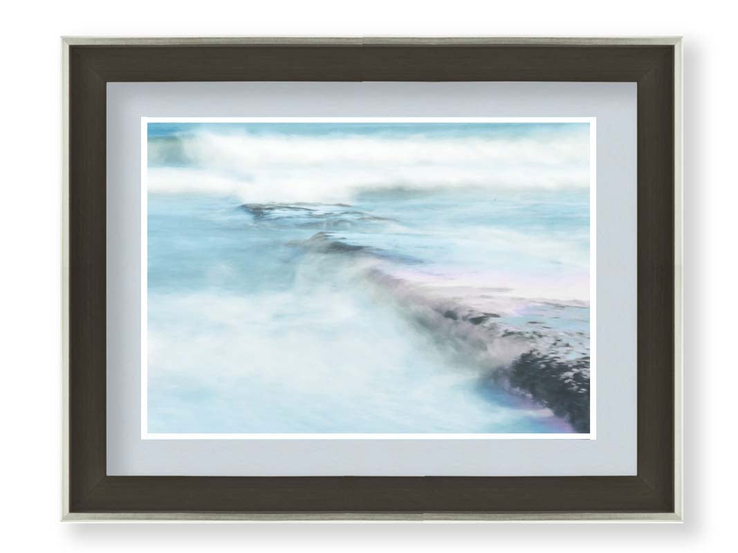 A photograph of a battered jetty being washed over by incoming waves in a cool, white and blue palette. Printed on paper, matted, and framed.