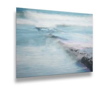 A photograph of a battered jetty being washed over by incoming waves in a cool, white and blue palette. Printed on metal.