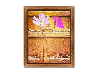 A photograph of two purple flowers in front of wooden steps, with all but the flower petals edited with a sepia tone. Printed on canvas and framed.