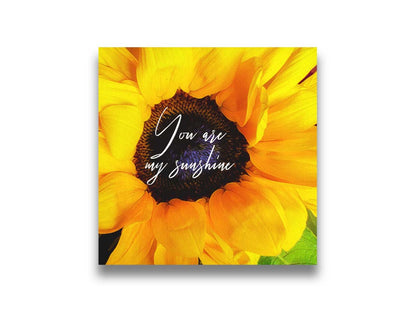 A closeup photo of a bright yellow sunflower, edited in a painterly style and overlaid with the quote "You are my sunshine." Printed on canvas.