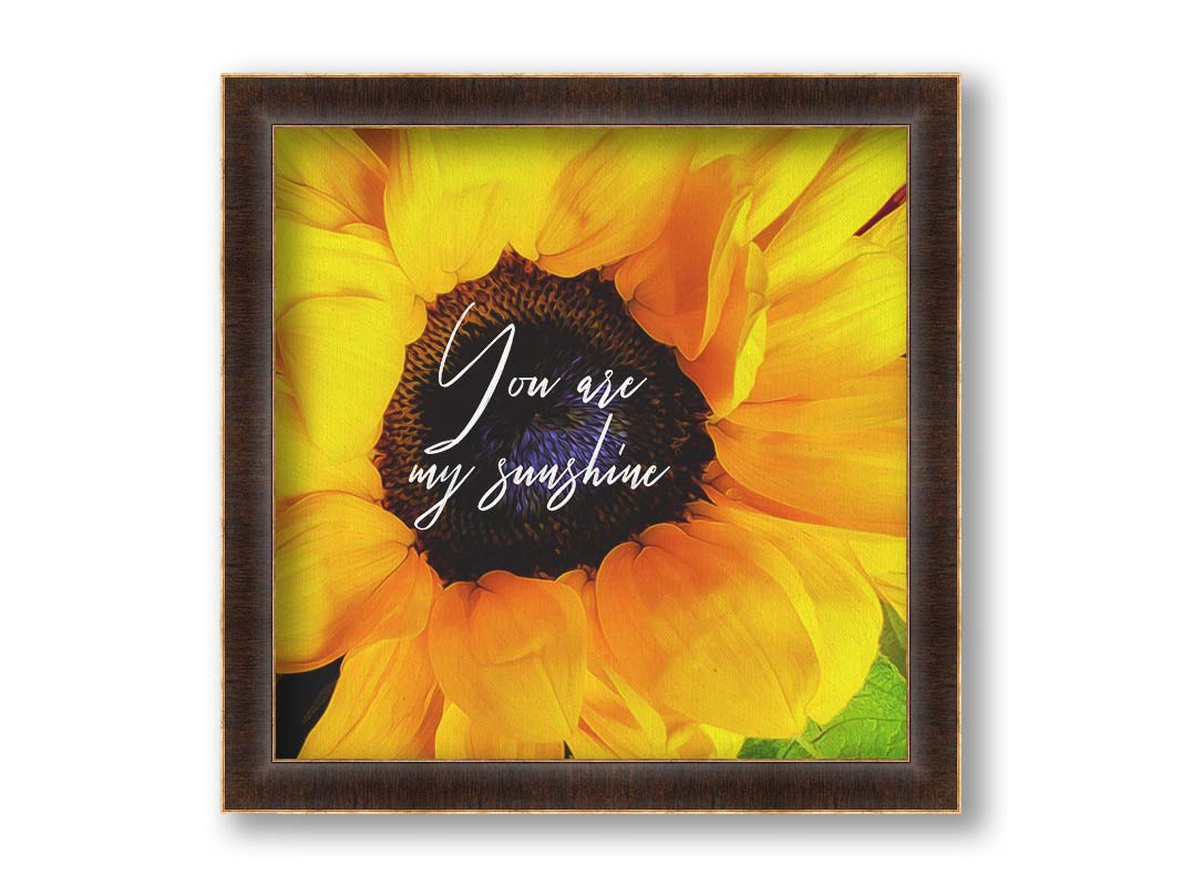 A closeup photo of a bright yellow sunflower, edited in a painterly style and overlaid with the quote "You are my sunshine." Printed on canvas and framed.