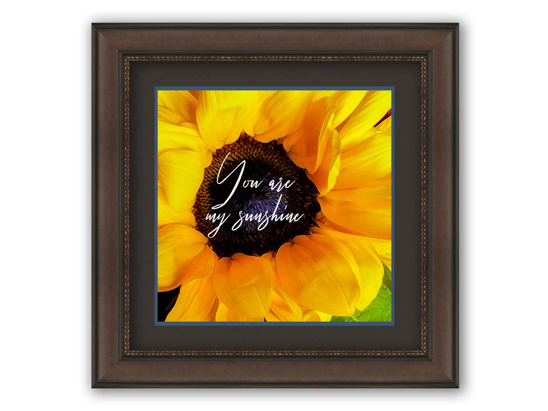 A closeup photo of a bright yellow sunflower, edited in a painterly style and overlaid with the quote "You are my sunshine." Printed on paper, matted, and framed.