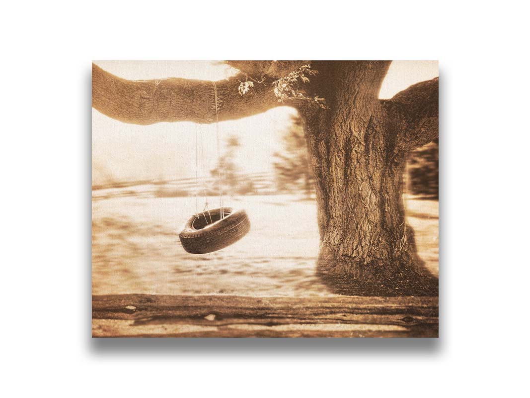 A sepia-tone photograph of a tire swing hanging from a sturdy tree in the daylight. Printed on canvas.