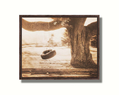 A sepia-tone photograph of a tire swing hanging from a sturdy tree in the daylight. Printed on canvas in a float frame.