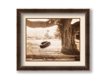 A sepia-tone photograph of a tire swing hanging from a sturdy tree in the daylight. Printed on paper, matted, and framed.