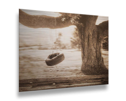 A sepia-tone photograph of a tire swing hanging from a sturdy tree in the daylight. Printed on metal.