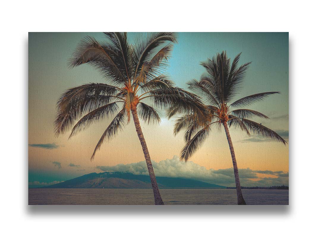 A photo of two palm trees in Maui at sunset, with the sea and cloud-topped mountains in the background. Printed on canvas.