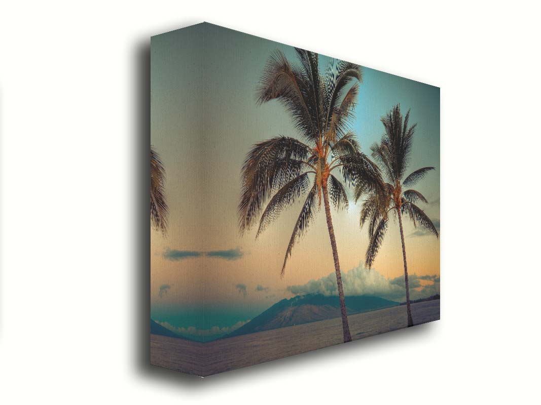 A photo of two palm trees in Maui at sunset, with the sea and cloud-topped mountains in the background. Printed on canvas.