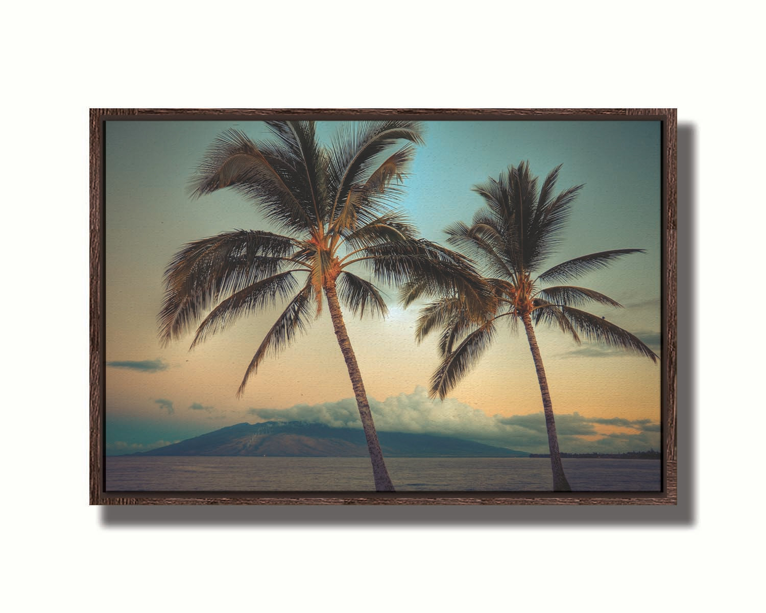 A photo of two palm trees in Maui at sunset, with the sea and cloud-topped mountains in the background. Printed on canvas in a float frame.