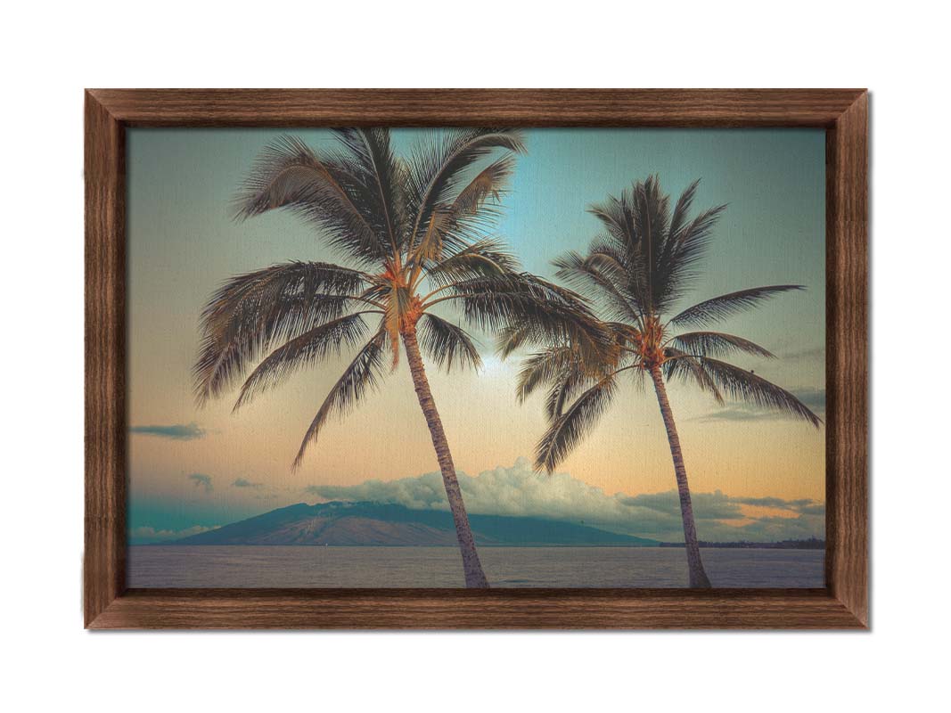 A photo of two palm trees in Maui at sunset, with the sea and cloud-topped mountains in the background. Printed on canvas and framed.