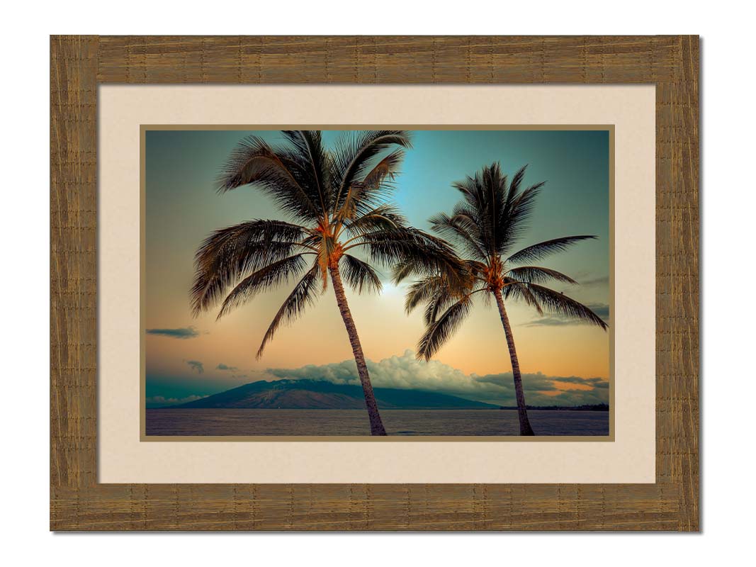 A photo of two palm trees in Maui at sunset, with the sea and cloud-topped mountains in the background. Printed on paper, matted, and framed.