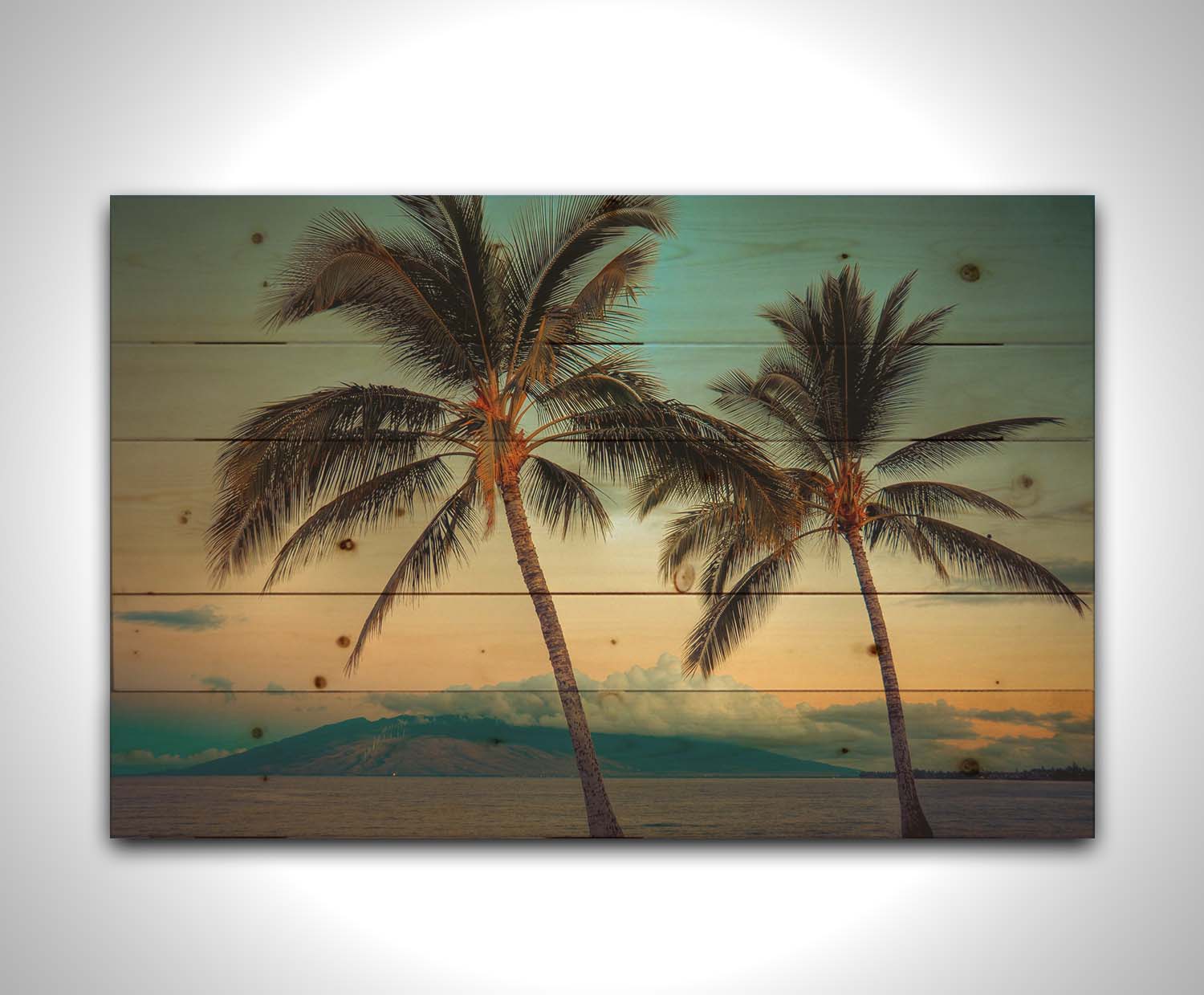 A photo of two palm trees in Maui at sunset, with the sea and cloud-topped mountains in the background. Printed on a wood pallet.