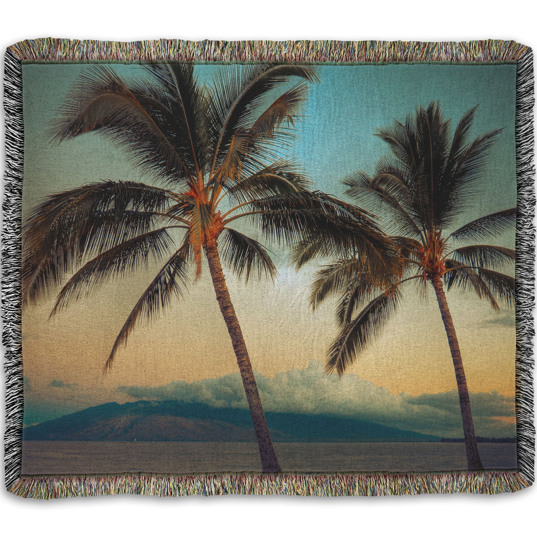 A woven throw blanket designed with a photo of two palm trees in Maui at sunset, with the sea and cloud-topped mountains in the background.