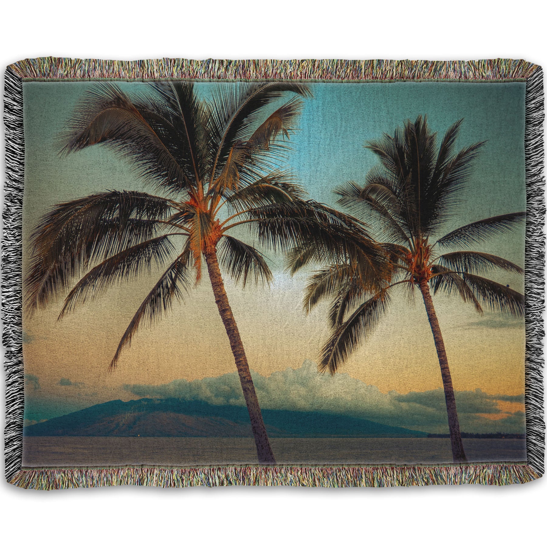 A woven throw blanket designed with a photo of two palm trees in Maui at sunset, with the sea and cloud-topped mountains in the background.