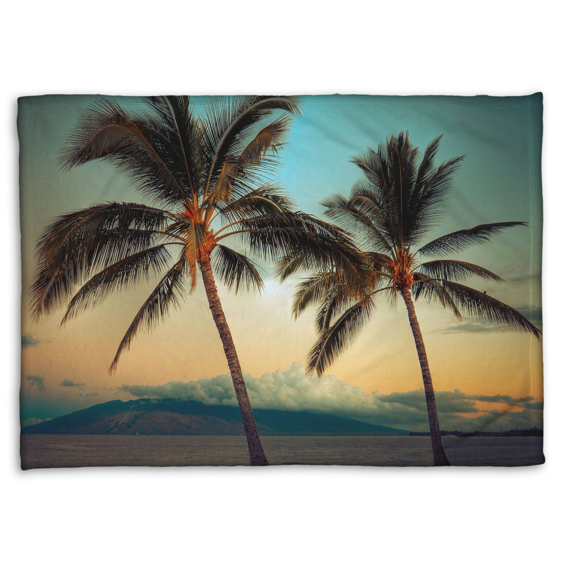 A coral fleece throw blanket designed with a photo of two palm trees in Maui at sunset, with the sea and cloud-topped mountains in the background.
