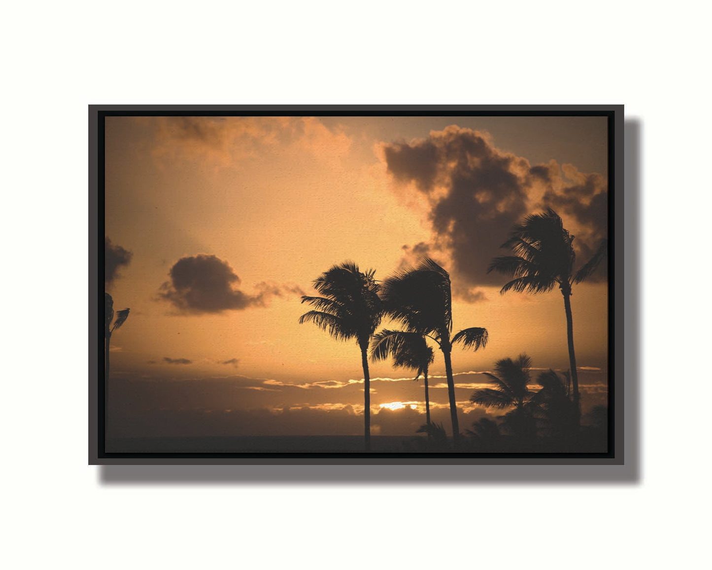 A photo of palm trees in Maui silhouetted by the setting sun, with the sea in the background. Printed on canvas in a float frame.