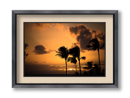 A photo of palm trees in Maui silhouetted by the setting sun, with the sea in the background. Printed on paper, matted, and framed.